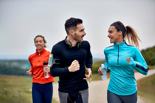 Happy athletic couple communicating while taking a part in marathon in nature.